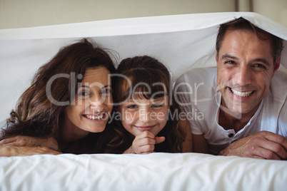 Parents and daughter smiling under the bed sheet