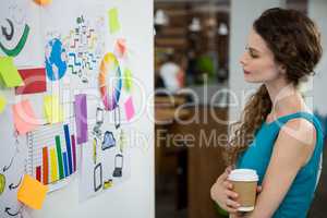 Thoughtful female executive looking at sticky notes on white wall