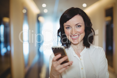 Portrait of female executive using mobile phone in corridor