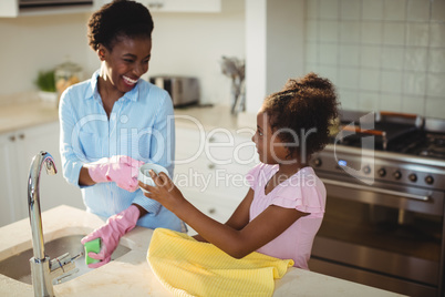 Mother assisting her daughter in cleaning utensils