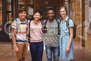 Portrait of happy students standing with arms around in corridor