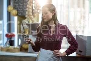 Smiling female staff using mobile phone at counter