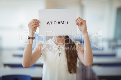 Schoolgirl holding white paper with text sign in classroom