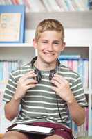 Portrait of happy schoolboy with digital tablet and headphones sitting in library