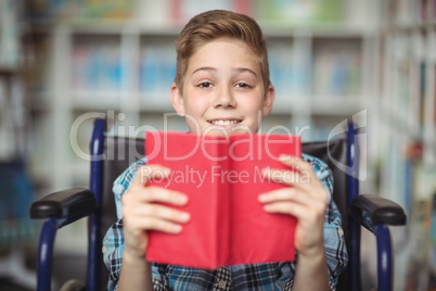 Portrait of disabled schoolboy holding book in library