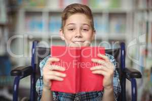 Portrait of disabled schoolboy holding book in library