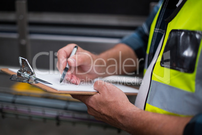 Male factory worker maintaining record on clipboard