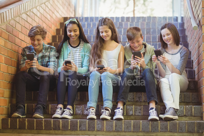 Group of smiling school friends sitting on staircase using mobile phone