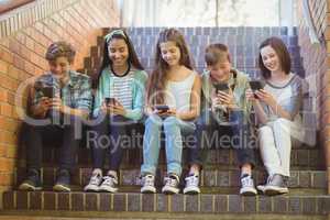 Group of smiling school friends sitting on staircase using mobile phone