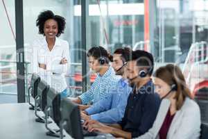 Smiling Businesswoman standing with arms crossed while colleagues talking on headset