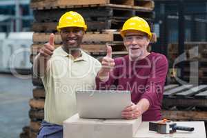 Two factory workers with laptop showing their thumbs up in drinks production plant