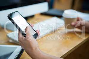 Female graphic designer holding disposable cup while using mobile phone