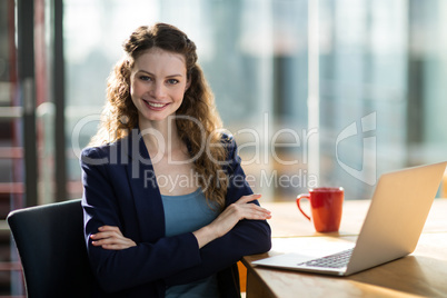 Portrait of female business executive sitting in office with laptop on table