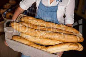 Mid-section of female staff holding basket of baguettes in bakery section