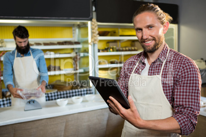 Portrait of smiling male staff using digital tablet near meat counter