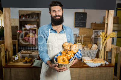 Portrait of smiling male staff holding a basket of bread at counter