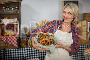 Smiling female staff holding wicker basket of pretzel bread at counter
