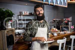 Smiling male staff using digital tablet at counter in coffee shop
