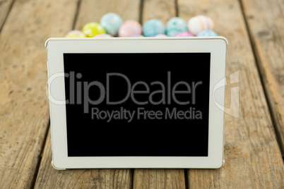 Painted Easter eggs and digital tablet on wooden surface
