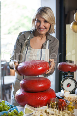 Portrait of female staff holding gouda cheese at counter
