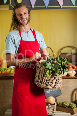 Smiling male staff holding leafy vegetables in basket at organic section