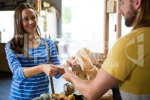Smiling female customer paying bill by cash at bread counter