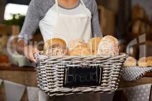 Female staff holding wicker basket of various breads at counter in bakery shop