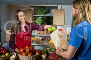 Smiling female staff offering fruits to customer at organic section