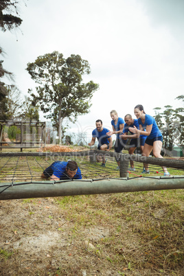 Fit man crawling under the net during obstacle course while fit people cheering