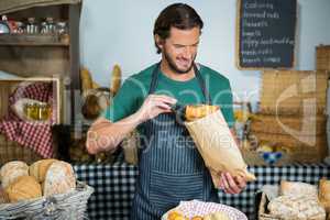 Smiling male staff packing bread in paper bag