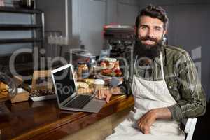 Smiling male staff using laptop at counter in bakery shop