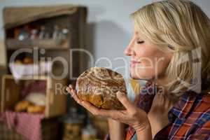 Smiling woman smelling a round loaf of bread at counter