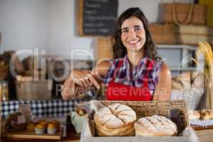 Smiling female staff holding wicker basket of breads at counter