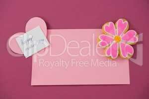 Flower shape cookie, heart shape card on red envelope against pink background