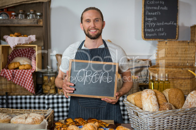 Portrait of smiling staff holding chalkboard with open sign at counter