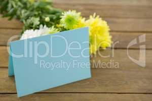 Bunch of yellow flowers with blank card on wooden plank