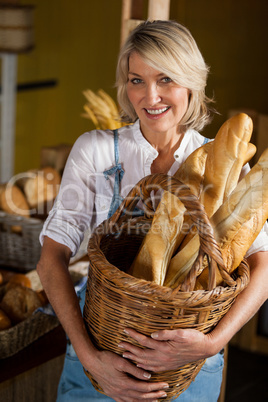 Female staff holding basket of baguettes in bakery section
