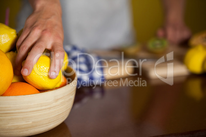 Mid-section of male staff picking a lemon fruit from a bowl