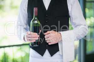 Male waiter holding bottle of wine in restaurant