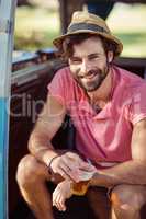 Portrait of happy man sitting in campervan with glass of beer