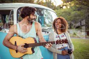 Man playing guitar near campervan while woman standing beside him