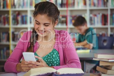 Smiling schoolgirl using mobile phone in library