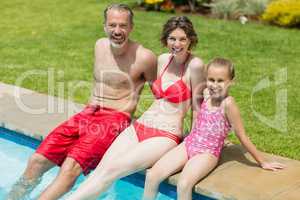 Portrait of parents and daughter sitting on poolside in pool water