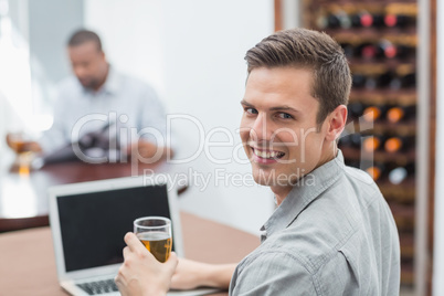 Handsome man holding beer glass while using laptop