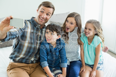 Smiling man taking selfie with family while sitting in bedroom