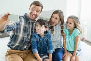 Smiling man taking selfie with family while sitting in bedroom