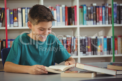 Smiling schoolboy reading book in library