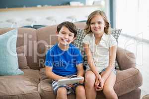Siblings using digital tablet on sofa in living room at home