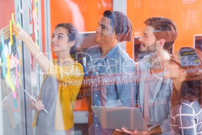 Smiling executives discussing over sticky notes on glass wall