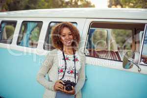 Woman leaning on campervan with camera